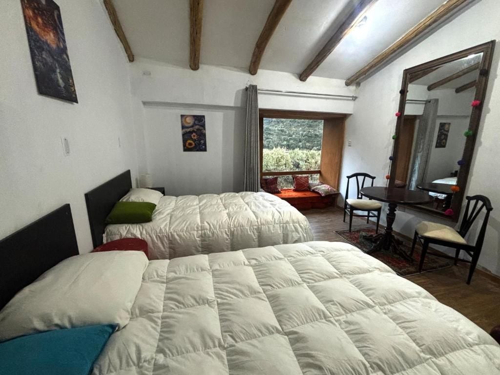 A bedroom with two beds, a window with a view, a mirror, and a small table with chairs.