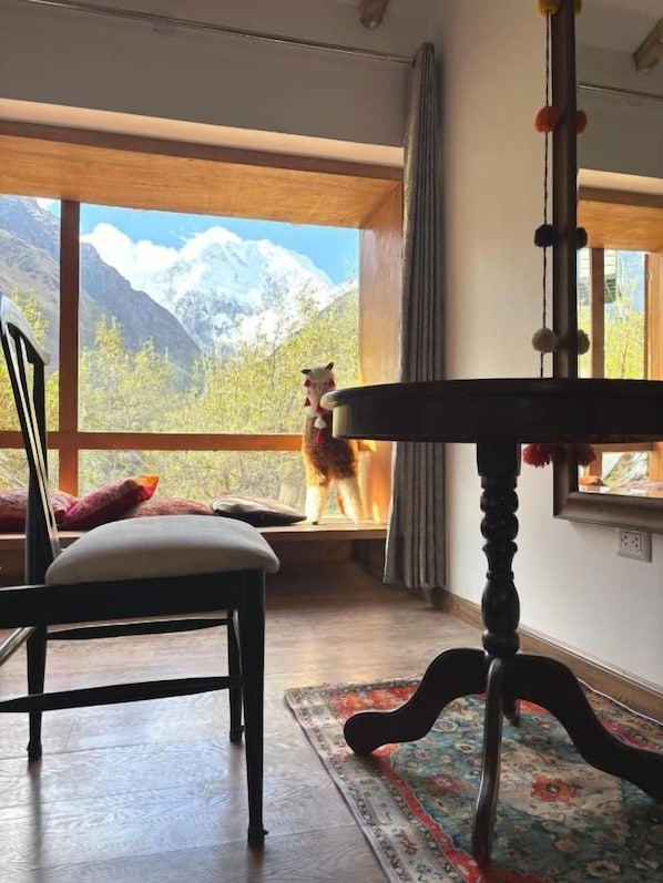 Une pièce avec une grande fenêtre, une table en bois, une chaise et un tapis.