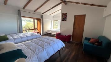 A bedroom with two beds, a red chair, a teal sofa, wooden beams on the ceiling, and a door.