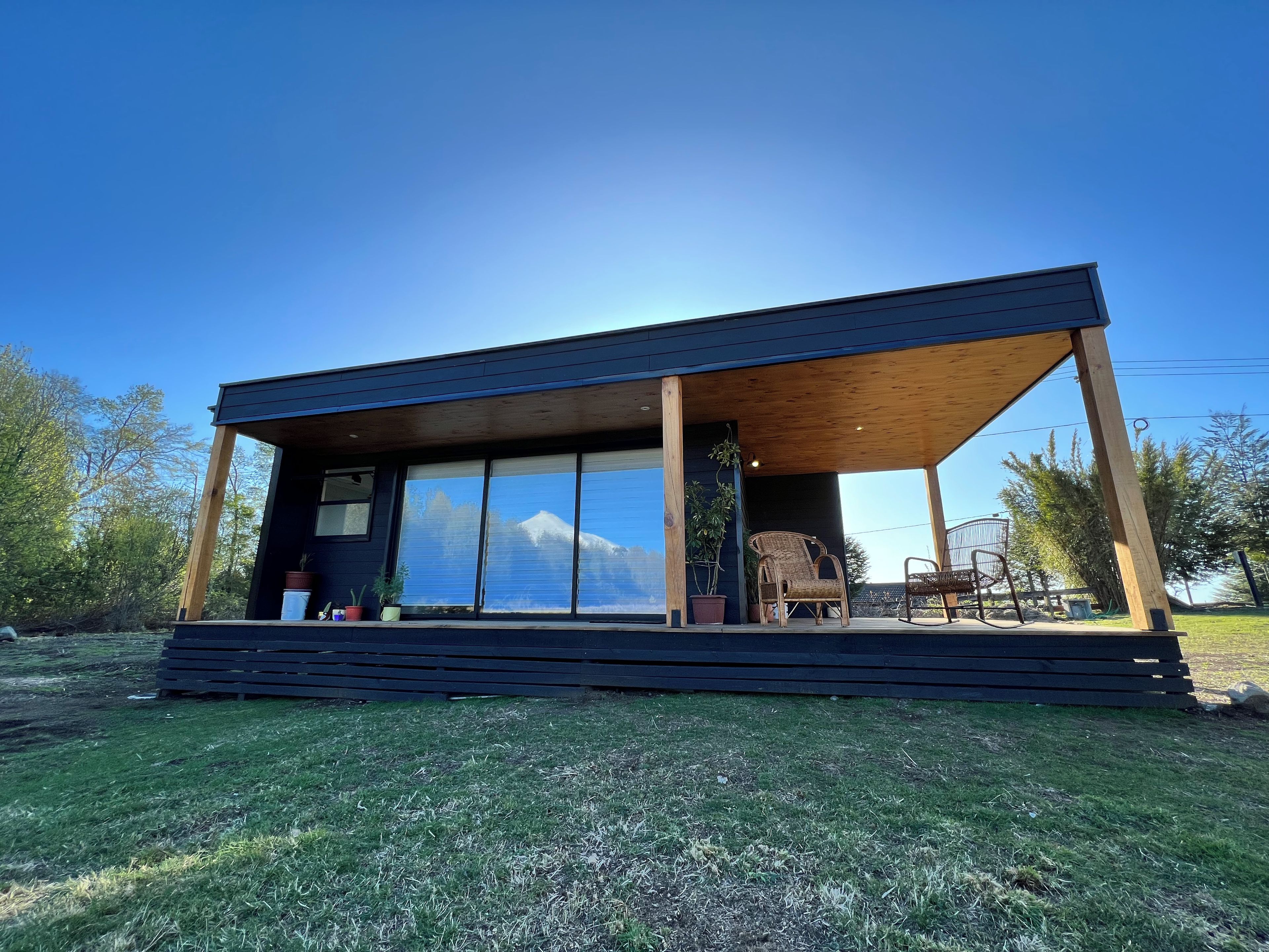 Une maison moderne dotée d’une grande baie vitrée, d’une terrasse en bois et offrant une vue sur la montagne.