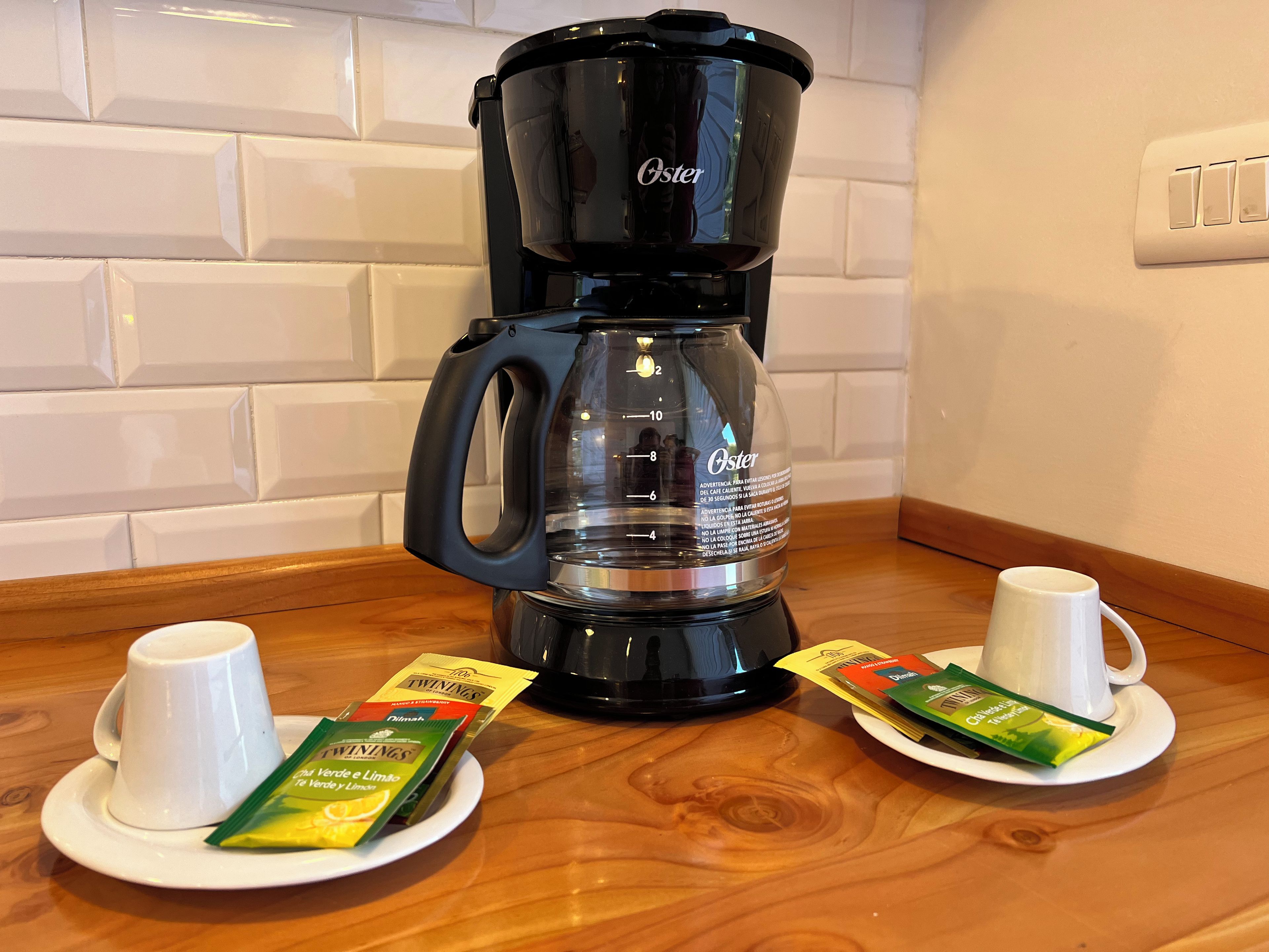 Eine schwarze Kaffeemaschine mit einem Glasbehälter, zwei weiße Tassen und Packungen Twinings Tee auf einem Holztisch.