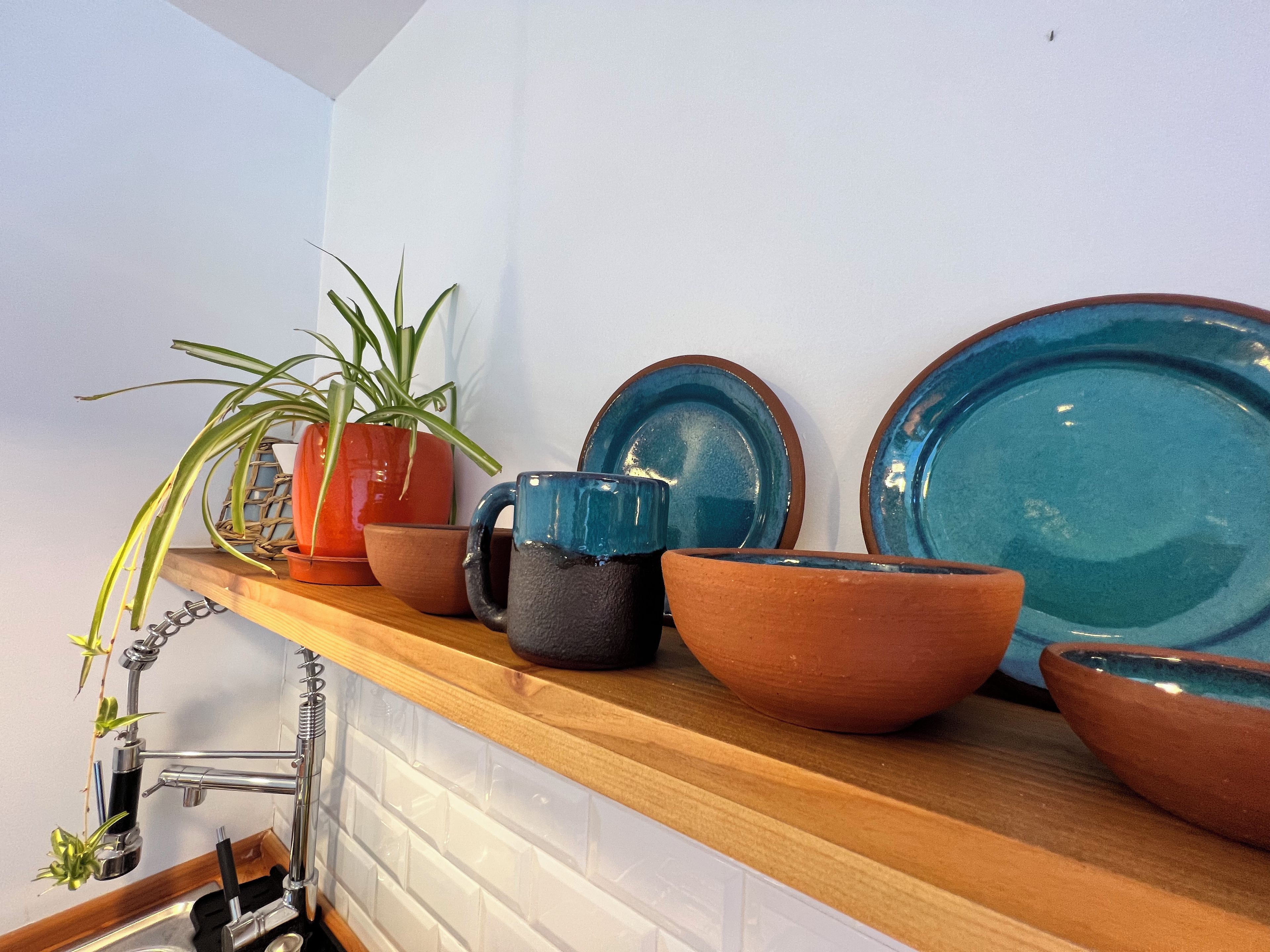 A kitchen shelf with various ceramic items, including a potted plant, a blue mug, and a large blue plate.