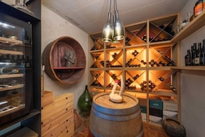 A wine cellar with wooden shelves and a barrel, illuminated by pendant lights.