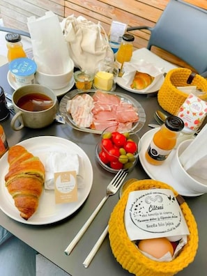 A breakfast table with croissants, ham, eggs, tomatoes, and beverages.