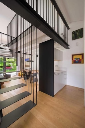 A modern interior with a staircase leading to a second floor, a kitchen area, and a dining space with a view of greenery outside.