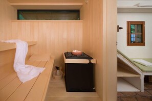 A sauna room with a wooden bench, a small heater, and a window.