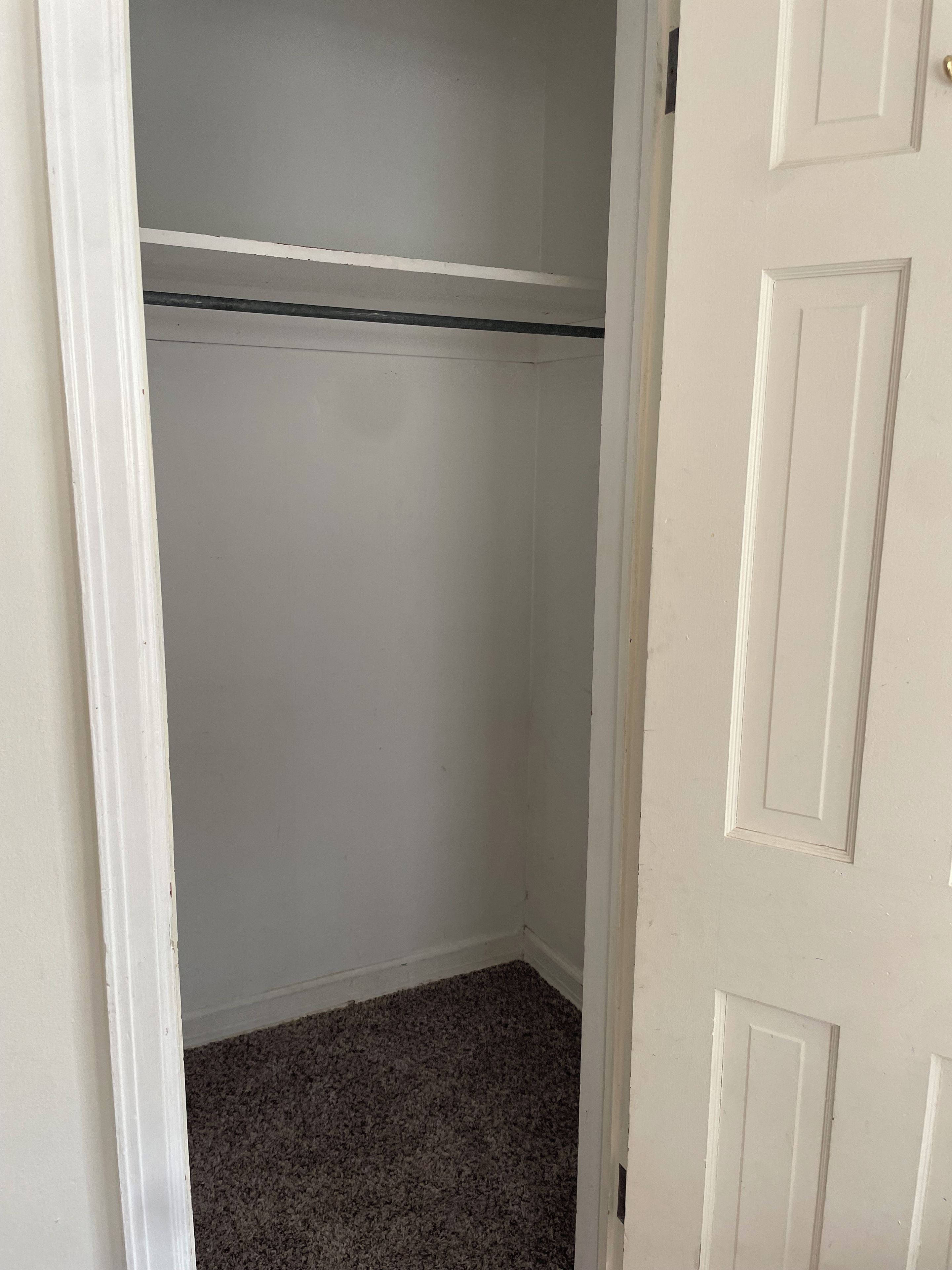 Een witte, gesloten deur met een eenvoudig ontwerp, die leidt naar een kamer met vloerbedekking en een witte muur.
