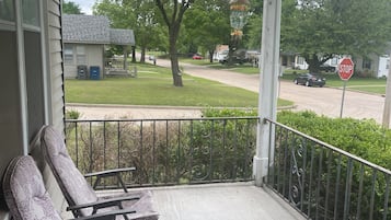 Een veranda met twee comfortabele stoelen, een stopbord en uitzicht op een woonstraat met huizen en een boom.