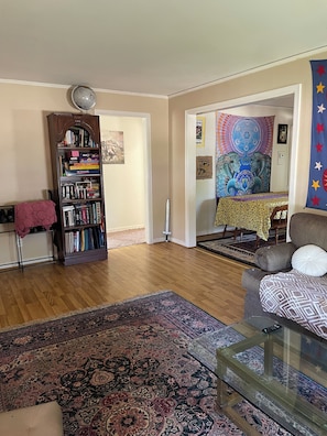 A living room with a wooden bookshelf, a patterned rug, a glass coffee table, and a blue star-patterned wall hanging.