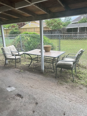 An outdoor patio with a table and chairs, a potted plant, and a view of a fenced yard.