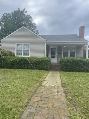 A single-story house with a front porch, a chimney, and a paved driveway.