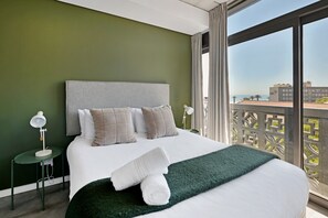 Una habitació d'hotel amb un llit gran, vista a la ciutat i un balcó amb barana.
