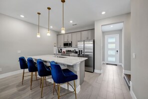 A modern kitchen with a central island, stainless steel appliances, and blue chairs.