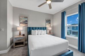 A hotel room with a bed, two bedside tables with lamps, a ceiling fan, artwork on the walls, and a window with curtains.