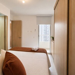 Ein Hotelzimmer mit Bett, Fenster mit Blick auf Gebäude, Schrank und Tür.