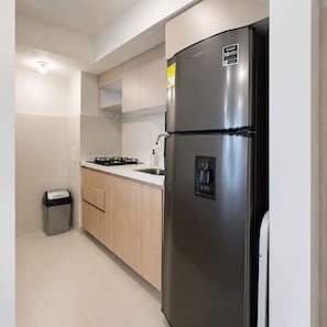 Eine kleine Küche mit einem Edelstahlkühlschrank, einem Gasherd und Holzschränken.