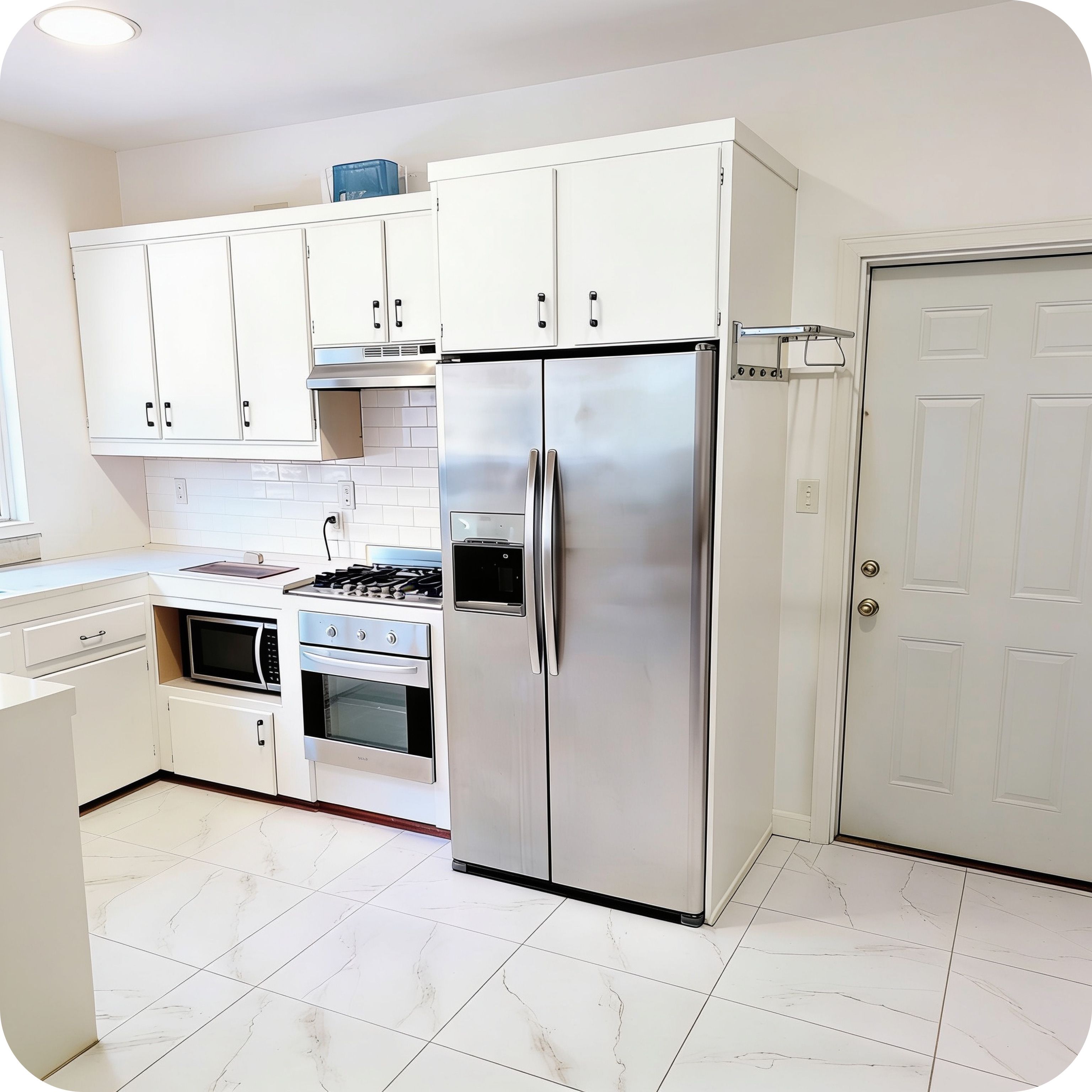 Una cocina con armarios blancos, un refrigerador de acero inoxidable, un horno y un microondas.