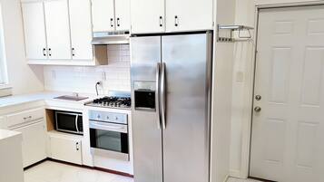 Una cocina con armarios blancos, un refrigerador de acero inoxidable, un horno y un microondas.