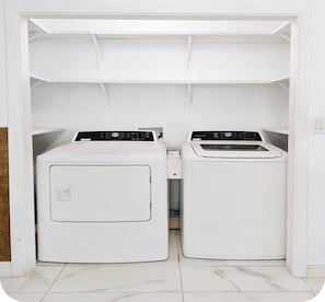 A laundry room with two white washing machines and a dryer, enclosed by a white cabinet with shelves.