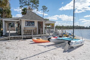 Een gebouw aan het strand met een steiger, kajaks en een zeilboot.