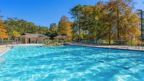 Ein Swimmingpool mit Liegestühlen und einer Laube, umgeben von Bäumen und einem Zaun.