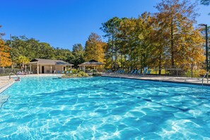 Ein Swimmingpool mit Liegestühlen und einer Laube, umgeben von Bäumen und einem Zaun.