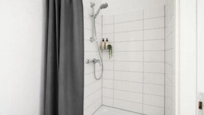 A bathroom with white tiled walls, a shower with a handheld showerhead, and a toilet. - Frechen Prime 1 (Frechen)