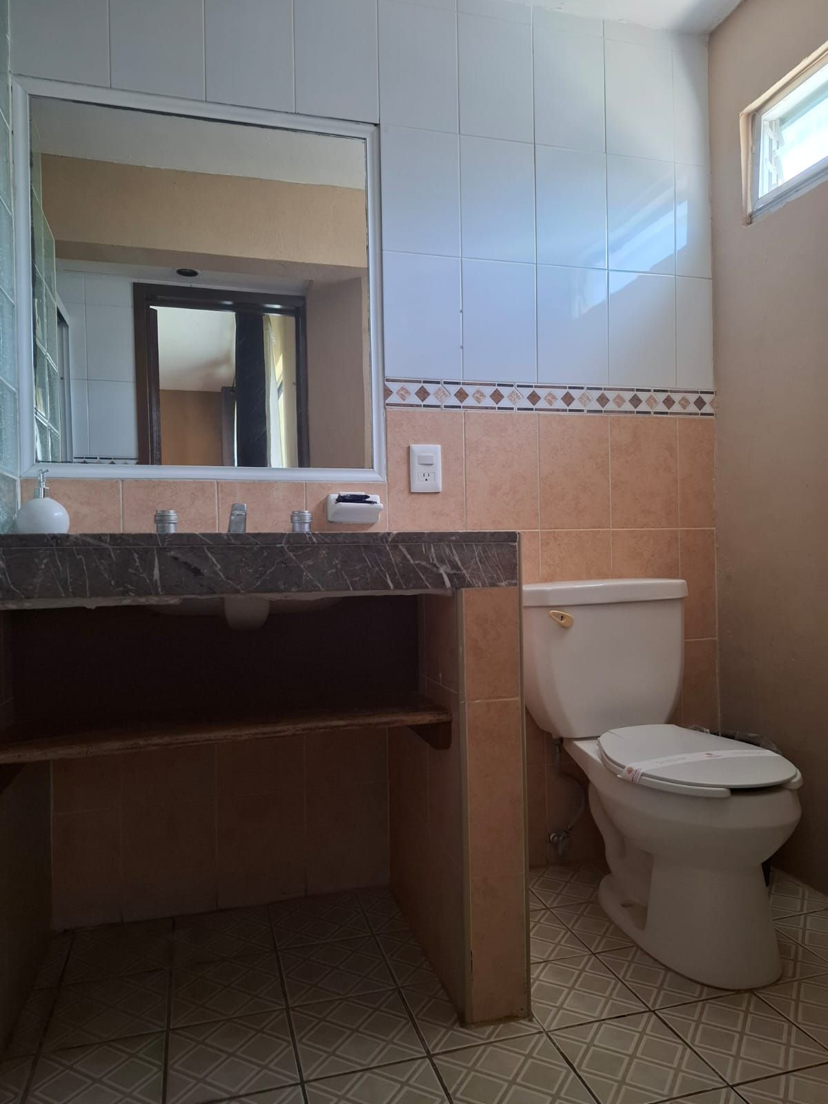 A bathroom with a marble countertop, a sink, a toilet, and a mirror.