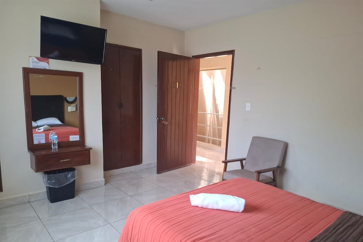 A hotel room with a bed, a chair, a TV, a wardrobe, and a door leading to a balcony.