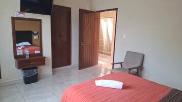 A hotel room with a bed, a chair, a TV, a wardrobe, and a door leading to a balcony.