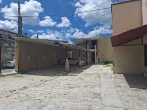 A narrow alleyway with a car parked on the left, a building with numbered parking spaces, and a red awning on the right.
