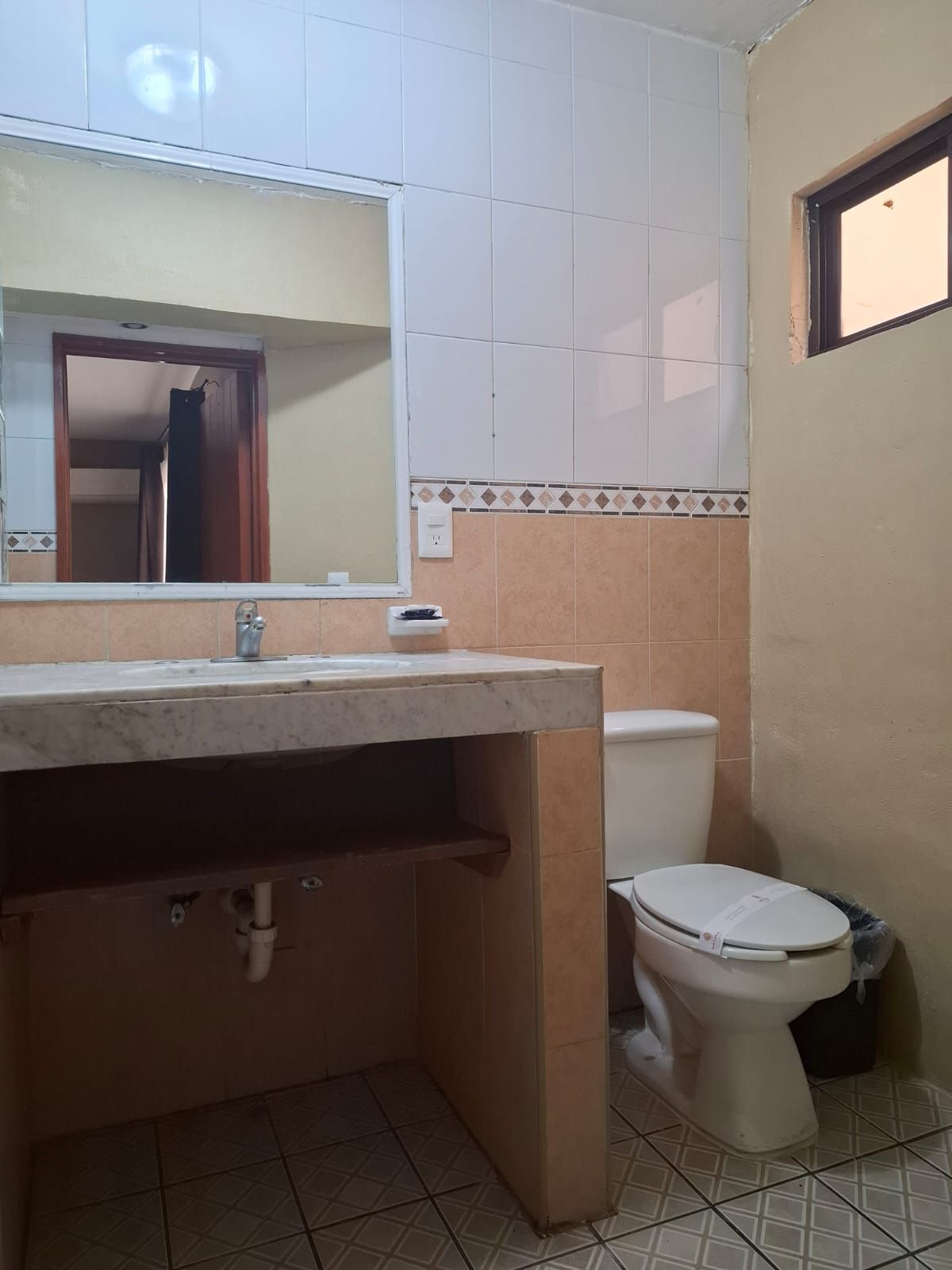 Un baño con lavamanos, espejo, inodoro y paredes con azulejos.