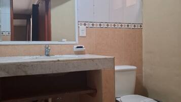 Un baño con lavamanos, espejo, inodoro y paredes con azulejos.
