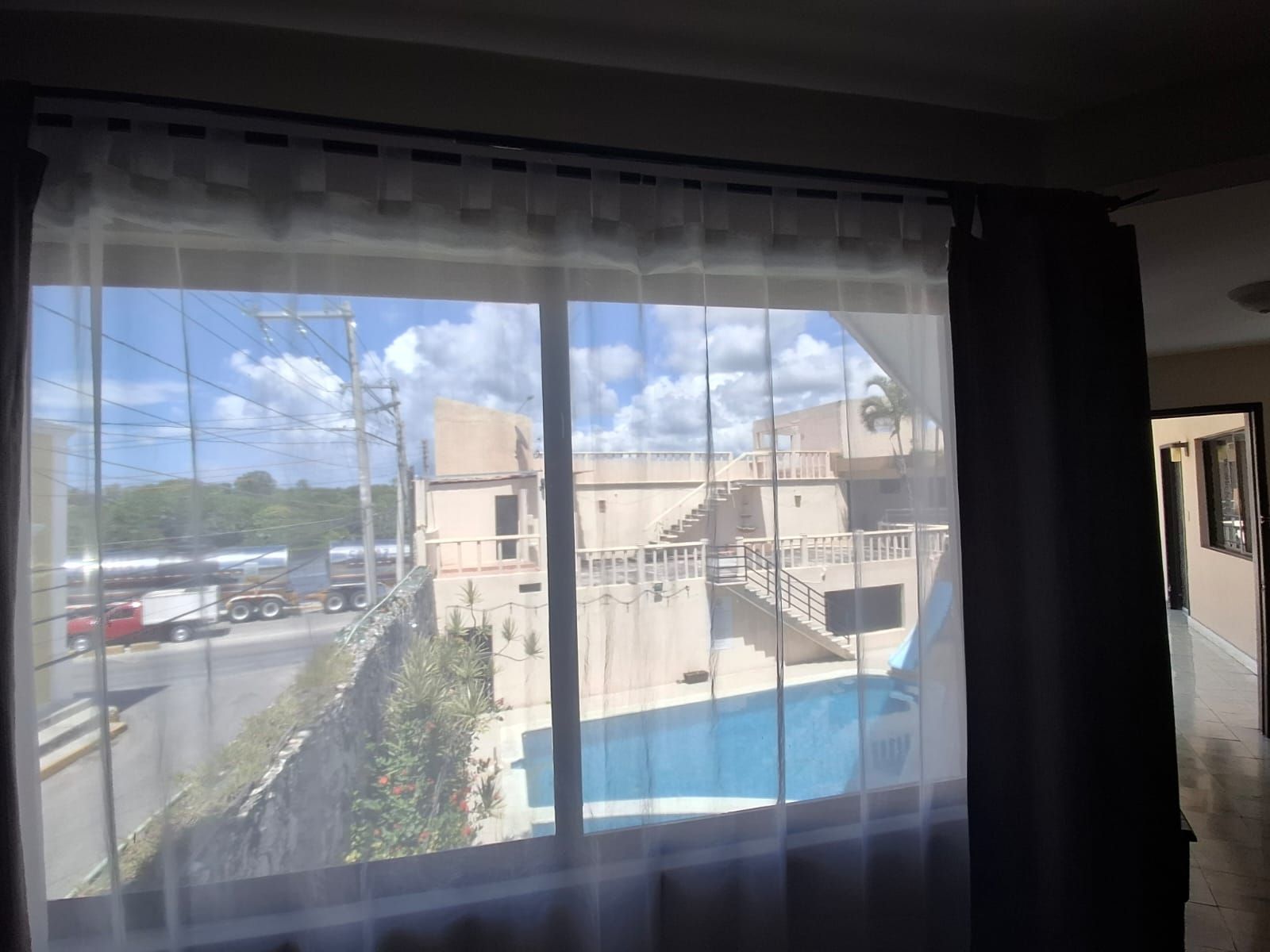 Habitación con ventana grande que da a una piscina y una calle con vehículos.