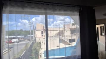 Habitación con ventana grande que da a una piscina y una calle con vehículos.