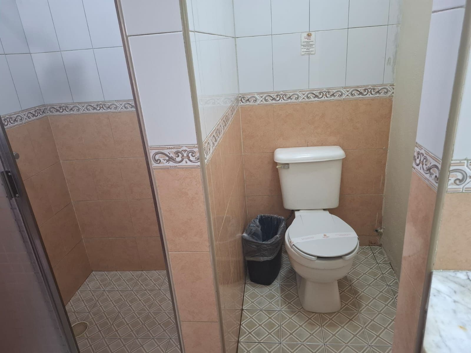 Un baño con inodoro, un cubo de basura y azulejos con diseño.