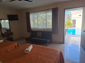 A hotel room with two beds, a sofa, a television, and a view of a swimming pool. - Hotel Aaktun Kay (Champotón)