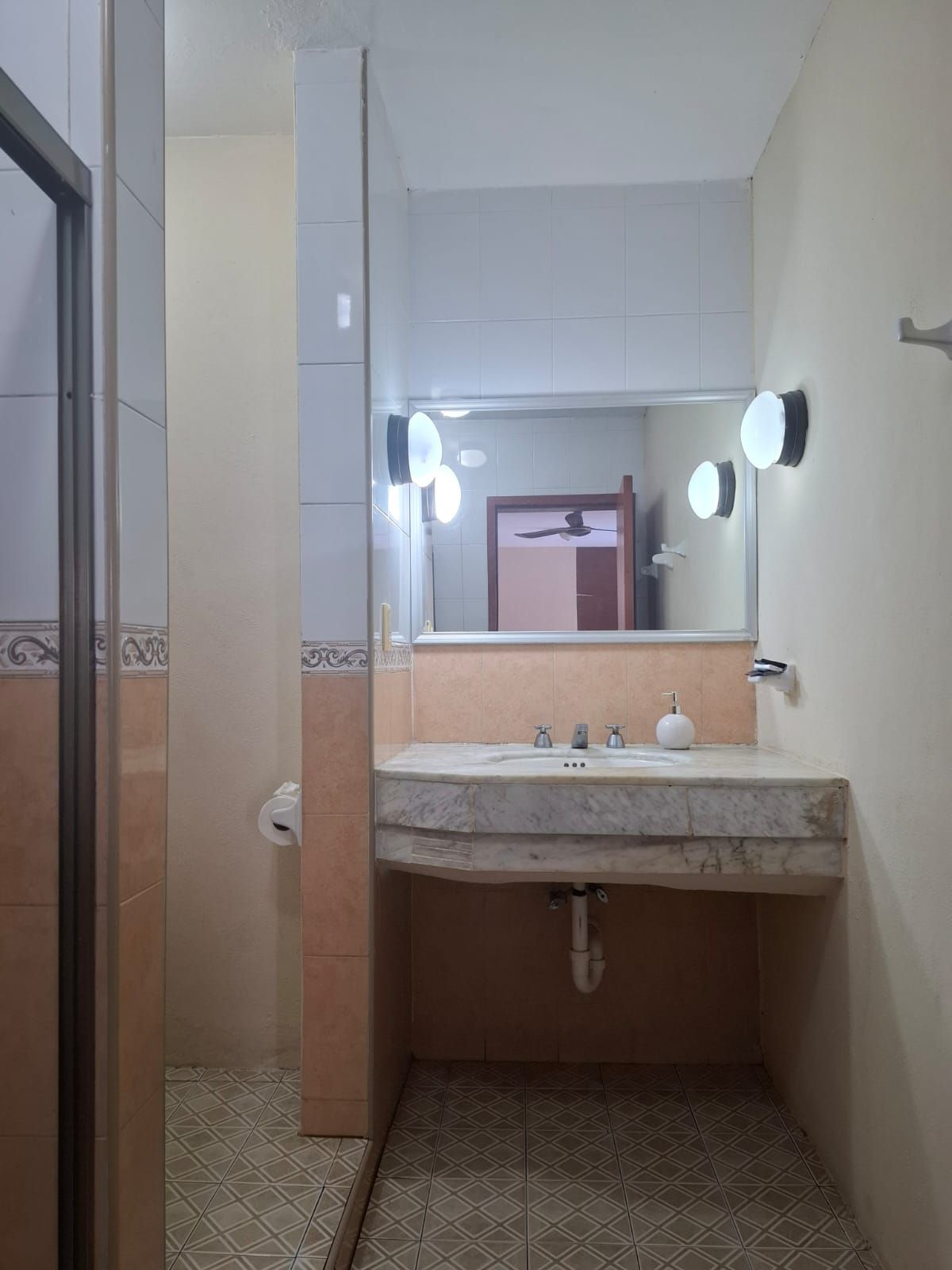 Un baño con lavamanos de mármol, un espejo con iluminación, un inodoro y baldosas de suelo estampadas.