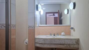 Un baño con lavamanos de mármol, un espejo con iluminación, un inodoro y baldosas de suelo estampadas.