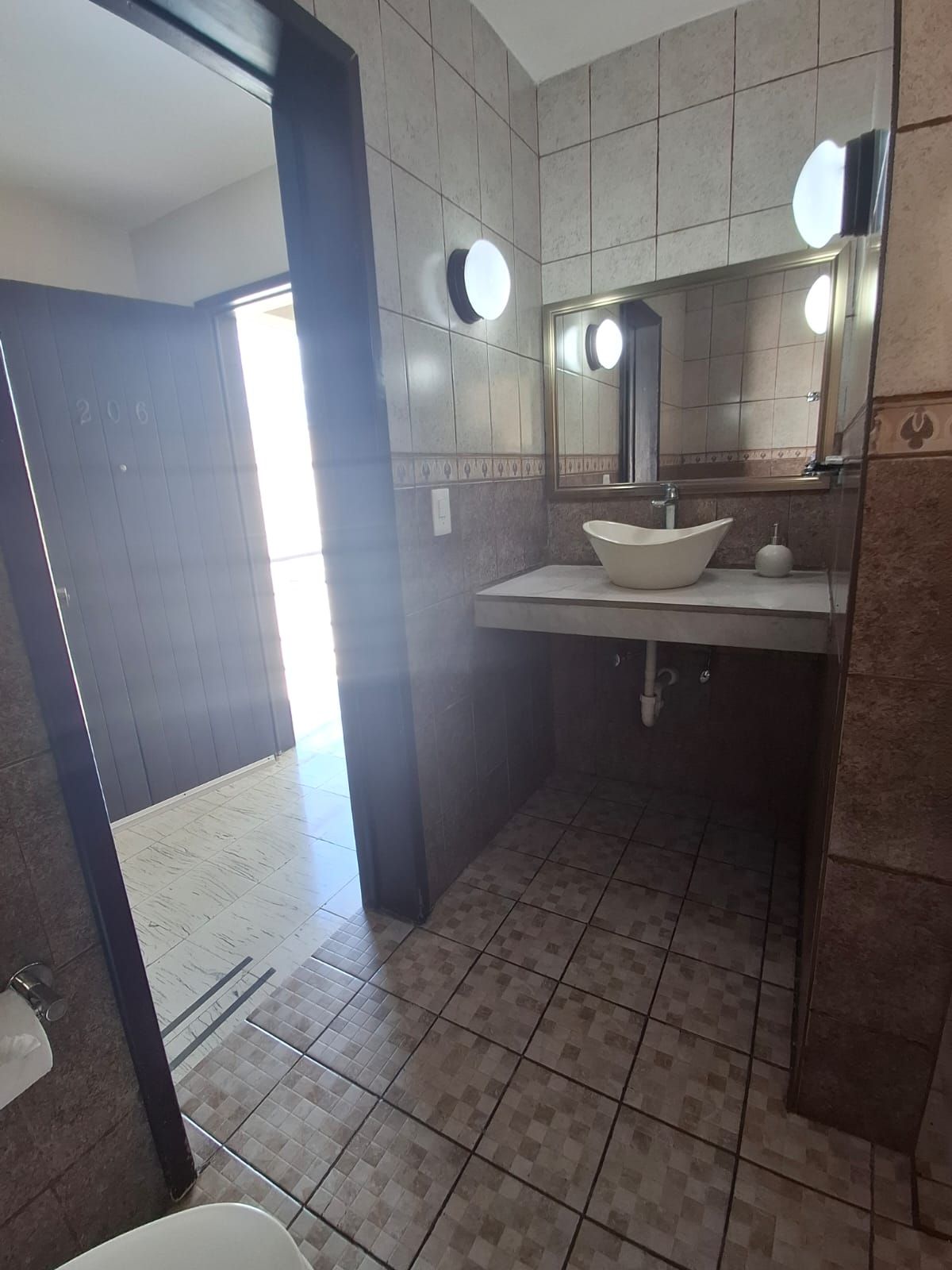 Un baño con un lavamanos blanco, un espejo y piso de azulejos.