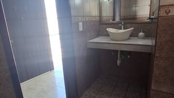 Un baño con un lavamanos blanco, un espejo y piso de azulejos.