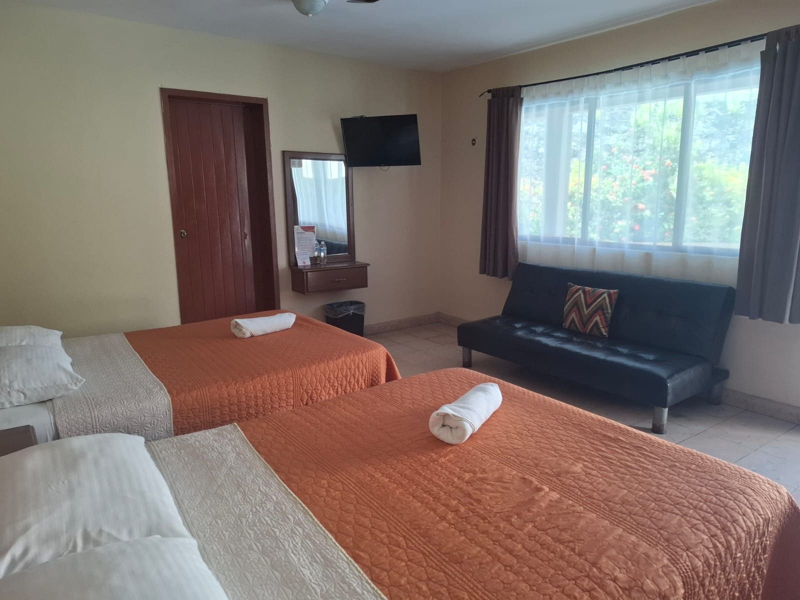 Habitación de hotel con dos camas, un sofá, un televisor y una ventana con cortinas.