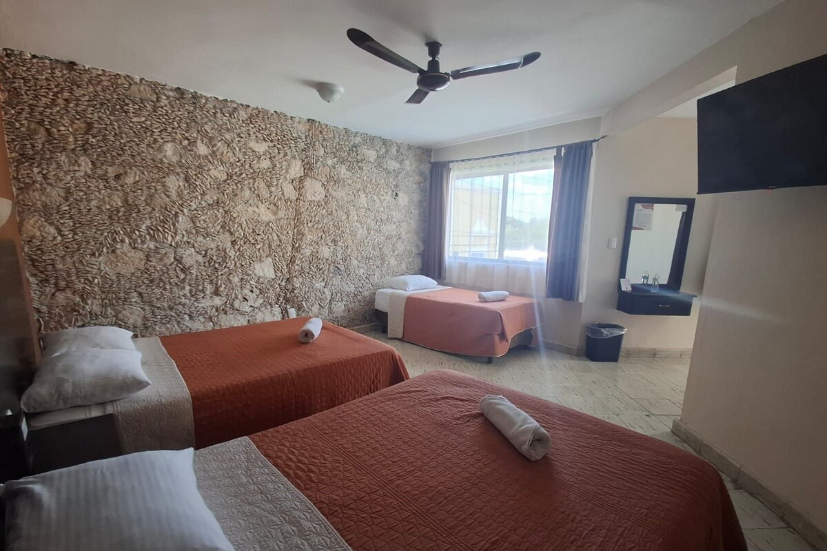 A hotel room with two beds, a stone wall, a ceiling fan, a window with curtains, and a sink.