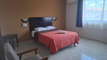 Una habitación de hotel con una cama, una silla, una mesita de noche y un ventanal con cortinas.