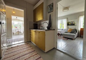 A modern kitchen with a central island, a dining area with a table and chairs, and a living room with a sofa and a painting. - Farmhouse with tiled stoves near lake and forest (Asarum)