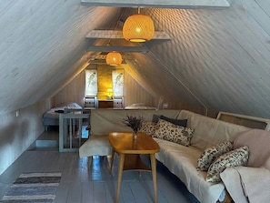 A cozy attic bedroom with a sloped ceiling, a wooden bed, a sofa, and a table with a vase. - Farmhouse with tiled stoves near lake and forest (Asarum)