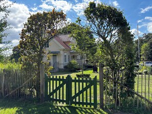 A house with a red roof, surrounded by a green fence, and a clear sky. - Farmhouse with tiled stoves near lake and forest (Asarum)
