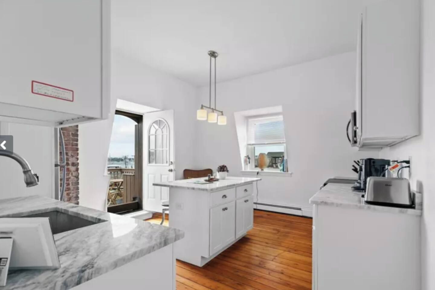 Une cuisine moderne avec des meubles blancs, un plan de travail en marbre et un luminaire suspendu.