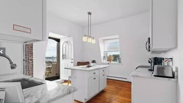 Une cuisine moderne avec des meubles blancs, un plan de travail en marbre et un luminaire suspendu.