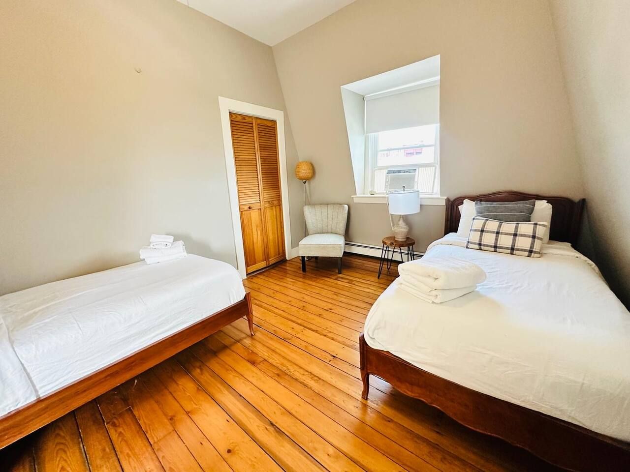 A room with two beds, a chair, and a window.